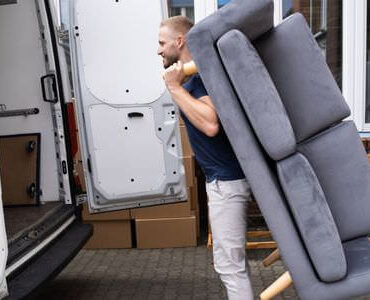 Möbellift Heidenheim Möbellift Heidenheim: Helfer tragen ein graues Sofa aus einem Transporter