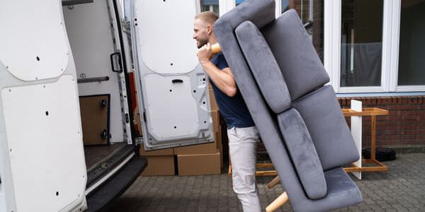Helfer tragen ein graues Sofa aus einem Transporter